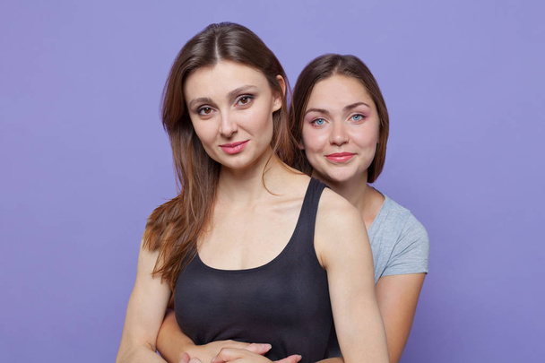 Two attractive young caucasian women standing huging, one besides another one. One with blue eyes, another one with dark brown, the both are brunettes. Isolated, studio, models. Emotions, laughing, smiling. - Fotó, kép