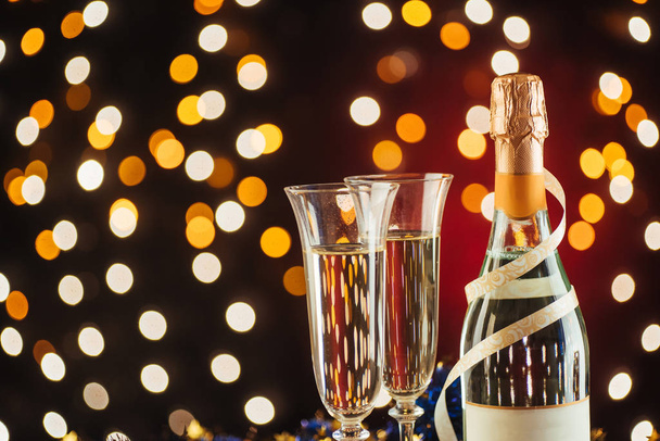 Christmas and New Year celebration with champagne. Pair of flute and bottle of Champagne for festive occasions against a dark background with gold shimmering light and bokeh - Foto, imagen