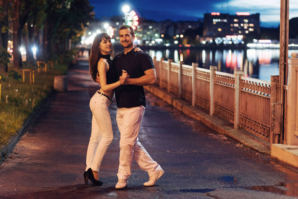 young couple dancing tango on the embankment of the river in the evening - Foto, Imagen