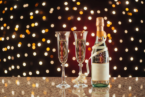 Christmas and New Year celebration with champagne. Pair of flute and bottle of Champagne for festive occasions against a dark background with gold shimmering light and bokeh - 写真・画像