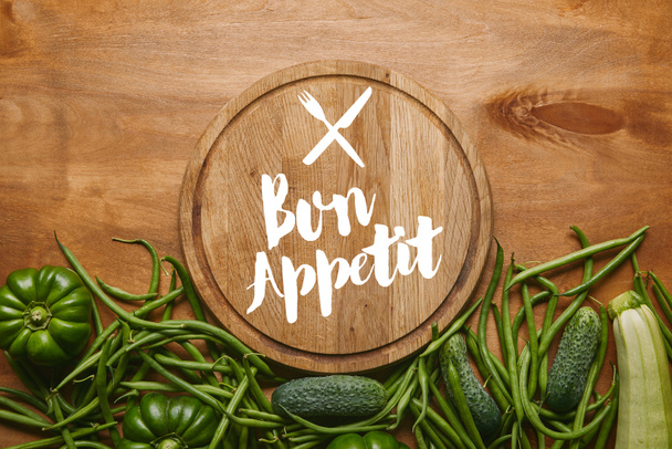 Cutting board with "bon appetit" lettering with green vegetables on wooden table - Φωτογραφία, εικόνα