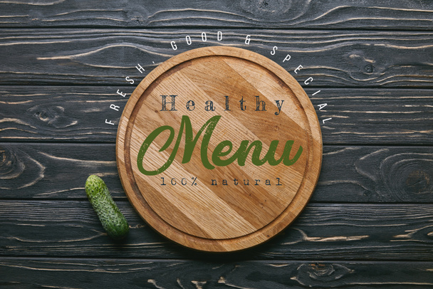 Cutting board with "healthy menu" lettering and cucumber on dark wooden table - Foto, Imagem