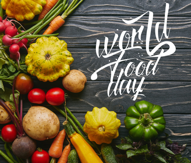 Органические сырые овощи на тёмном деревянном столе с надписью "Всемирный день еды"
 - Фото, изображение