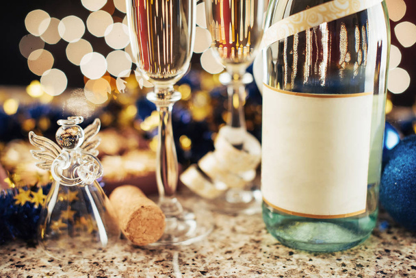 Γιορτή Χριστουγέννων και Πρωτοχρονιάς με σαμπάνια. Ζευγάρι φλάουτο και μπουκάλι σαμπάνιας για εορταστικές εκδηλώσεις σε σκούρο φόντο με χρυσό φως αστραφτερό και bokeh - Φωτογραφία, εικόνα