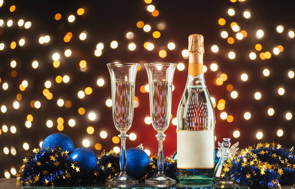 Christmas and New Year celebration with champagne. New Year holiday decorated table. Two Champagne Glasses against a dark background with gold shimmering light and bokeh - Foto, Imagen
