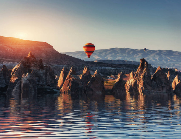 Composition of balloons over water and valleys, gorges, hills, between the volcanic mountains at sunset. Cappadocia, Turkey - Valokuva, kuva