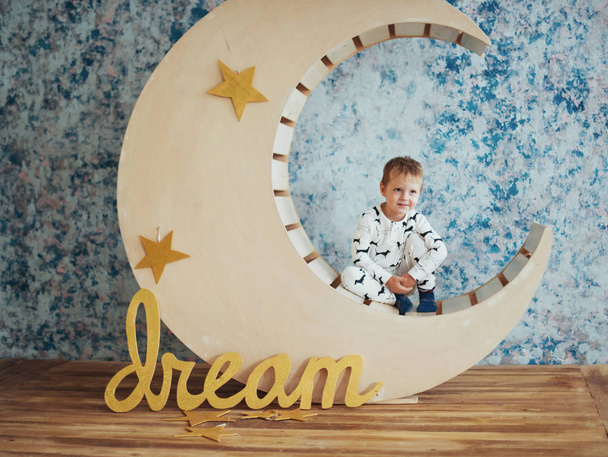 Дитина в м'якій і теплій піжамі лежить на дерев'яних місяцях з зірками в студії
 - Фото, зображення