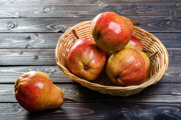 Bright red-yellow pears in a basket on a dark wooden rustic background. Autumn harvest of fruits. - Foto, Bild