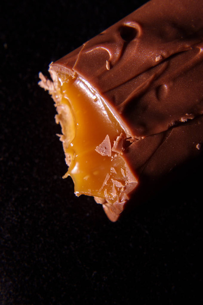 Откуси шоколадную плитку с карамельным макро крупным планом на черном фоне
 - Фото, изображение
