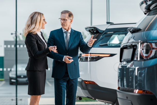 businessman and businesswoman choosing new automobile in showroom - Fotó, kép
