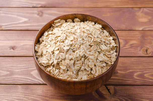Oat flakes in wooden bowl on wooden rustic background. - Foto, immagini