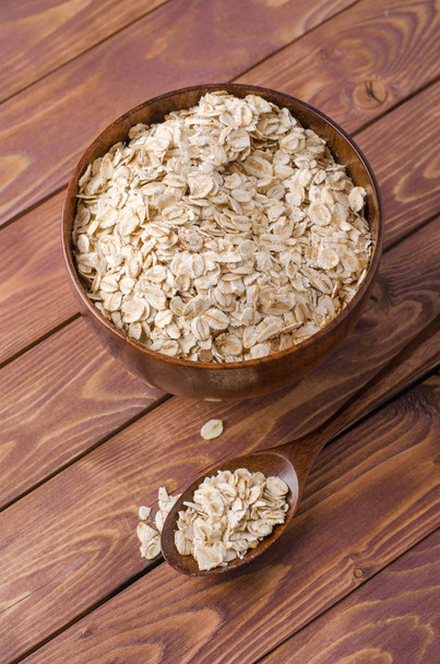 Oat flakes in wooden bowl on wooden rustic background. - Фото, изображение
