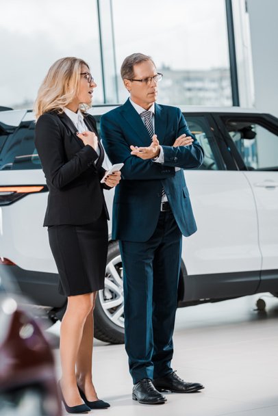 businessman and businesswoman with smartphone choosing new automobile in showroom - Fotoğraf, Görsel