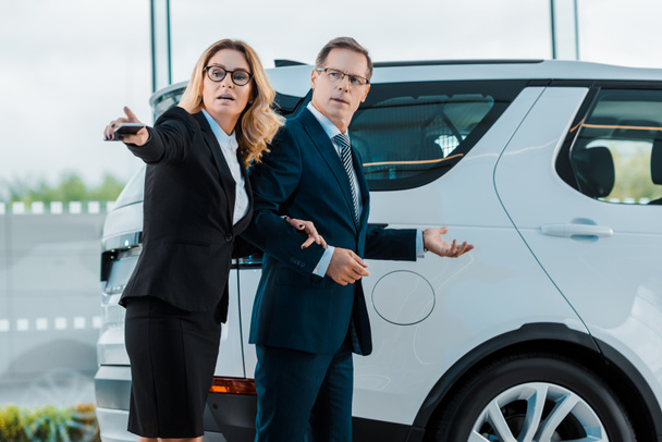 businessman and businesswoman pointing away while choosing new automobile in showroom - Foto, afbeelding