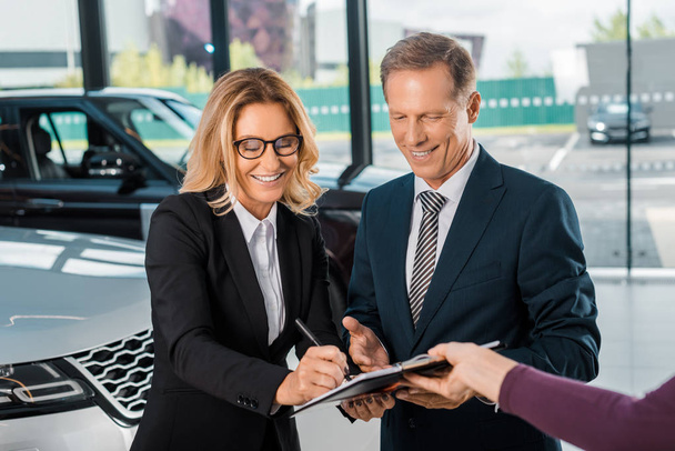 heureux couple d'affaires signer des papiers pour acheter une nouvelle voiture dans le showroom
 - Photo, image