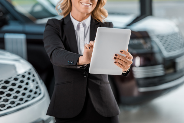 cropped shot of smiling female car dealer holding tablet in showroom - Fotoğraf, Görsel
