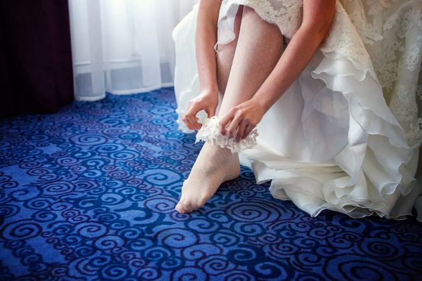 Jarreteira na perna de uma noiva, noiva sexy magro em vestido de luxo casamento mostrando sua liga de seda. mulher tem uma preparação final para a cerimônia de casamento. Momentos do dia do casamento
 - Foto, Imagem