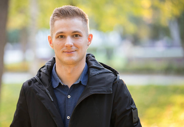 Handsome and young man in a black jacket standing in the park. Portrait - Photo, Image