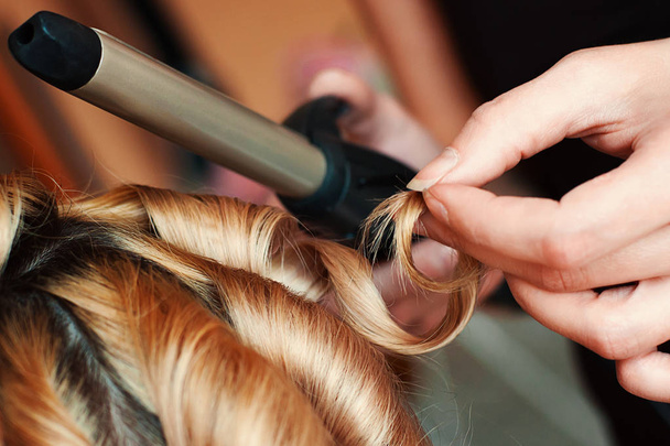 Gros plan des mains de coiffeur professionnel au salon de beauté, bouclant les cheveux féminins
 - Photo, image