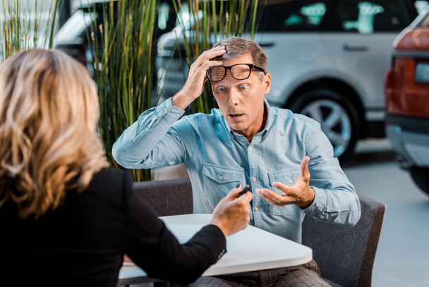 shocked adult customer and female car dealer sitting in showroom - Photo, Image