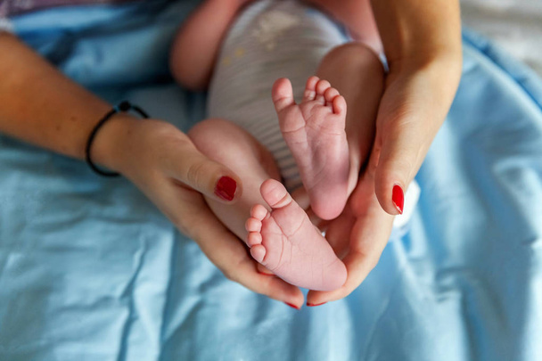 Pies de bebé en manos de madre. Pequeños pies del bebé recién nacido en manos femeninas en forma de primer plano. Mamá y su hijo. Concepto de familia feliz. Hermosa imagen conceptual de la maternidad - Foto, imagen