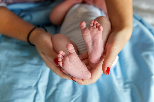 母親の手に赤ん坊の足。小さな新生児の赤ちゃんの足の女性の形をした手を閉じます。ママと子供だ。幸せな家族の概念。妊娠の美しい概念的なイメージ - 写真・画像