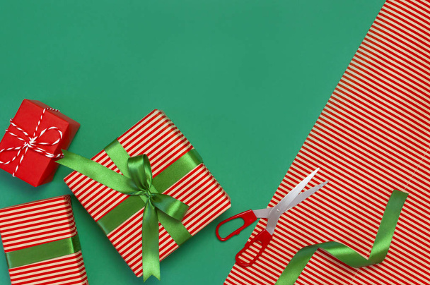 Gift boxes, packing paper, scissors, ribbon on green background. Festive background, congratulation, gift wrapping, Christmas and new year theme. Flat lay, top view - Fotografie, Obrázek