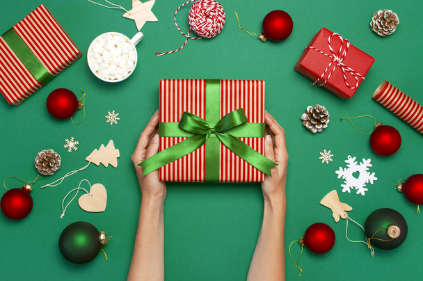 Женщина держит в руках коробку подарков, рождественские шары, игрушки, еловые шишки, ленту на зеленом фоне. Праздничные новогодние подарки Рождественские открытки 2019 года. Плоский лежал
 - Фото, изображение