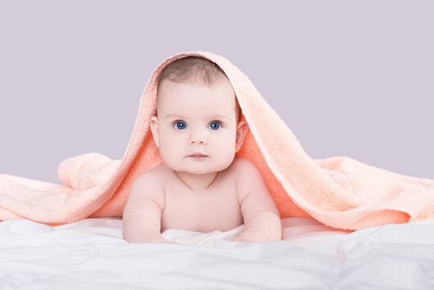 Bebê com grandes olhos azuis deitado na barriga sob a toalha rosa após o chuveiro, isolado sobre fundo cinza
 - Foto, Imagem