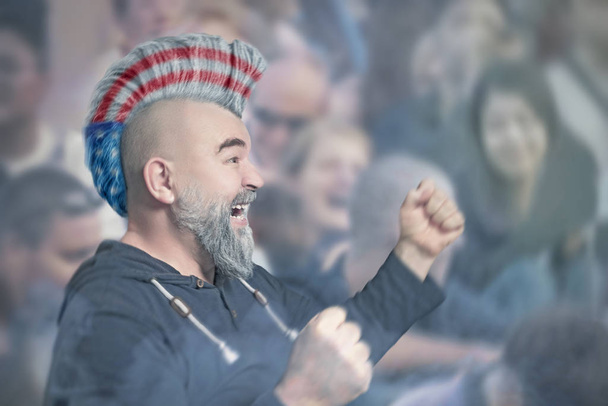 Deporte partidario con corte de pelo iroquesa en colores de la bandera de Estados Unidos durante un partido de fútbol o fútbol en el estadio
 - Foto, Imagen