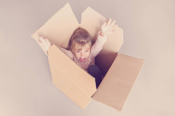 Llittle blonde girl screams inside a cardboard box. Toned - Foto, afbeelding