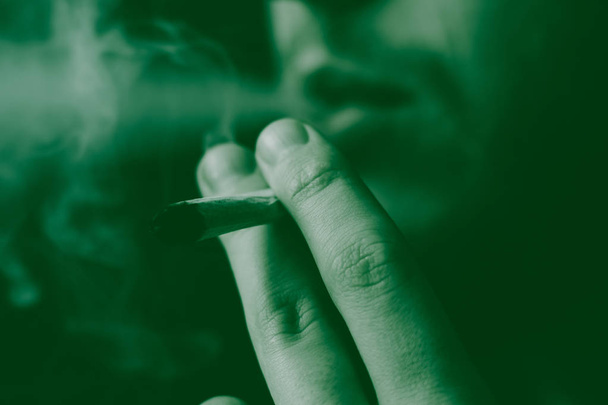косяк в руке. Человек курит марихуану. Дым на черном фоне. Концепции использования медицинской марихуаны и легализации марихуаны. На черном фоне
 - Фото, изображение