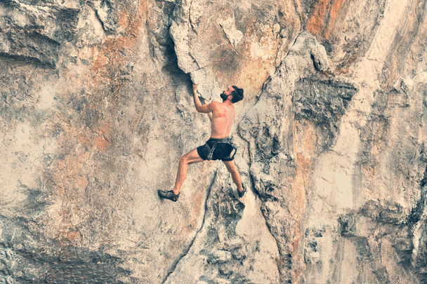 Ein junger bärtiger Mann klettert ohne Sicherungsseil die Klippe hinauf. gemildert - Foto, Bild