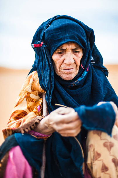 Портрет старой берберской женщины, сидящей на песчаной дюне в Мерзуге, Марокко
 - Фото, изображение
