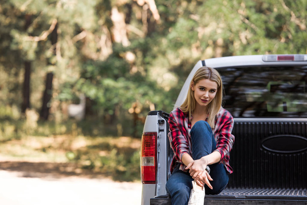 happy beautiful girl looking at camera and sitting on pickup truck in forest - 写真・画像