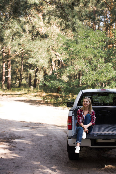happy young woman sitting on pickup truck in forest - Foto, Imagen