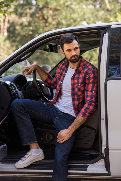 handsome bearded driver sitting in pickup truck in forest - Photo, Image