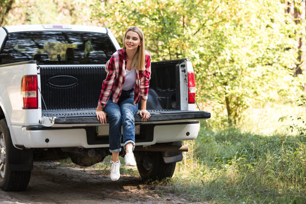 attractive young woman looking away and sitting in trunk of pick up car outdoors  - Foto, Imagen