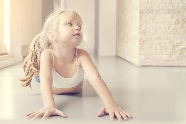Little blond girl doing stretching exercises in the sunny room - Фото, зображення