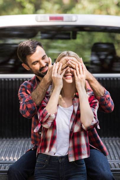 guapo novio cerrando ojos de feliz novia cerca de coche
 - Foto, Imagen
