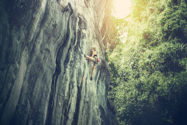 Jonge vrouw klimt een klif op een zonnige zomerdag - Foto, afbeelding
