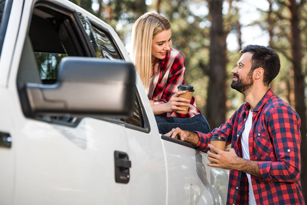 cheerful young couple with paper cups of coffee near pick up car outdoors  - Foto, Bild