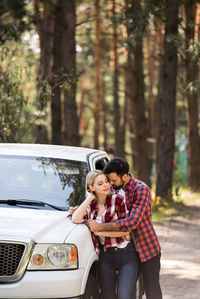 handsome boyfriend hugging his girlfriend near pickup truck in forest - 写真・画像