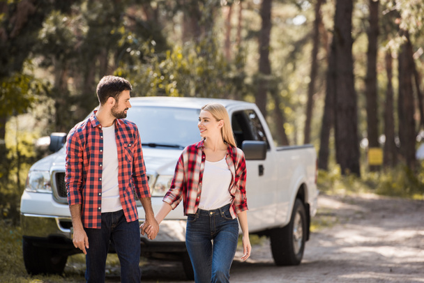 young couple holding hands and walking in forest with pickup truck  - Fotó, kép
