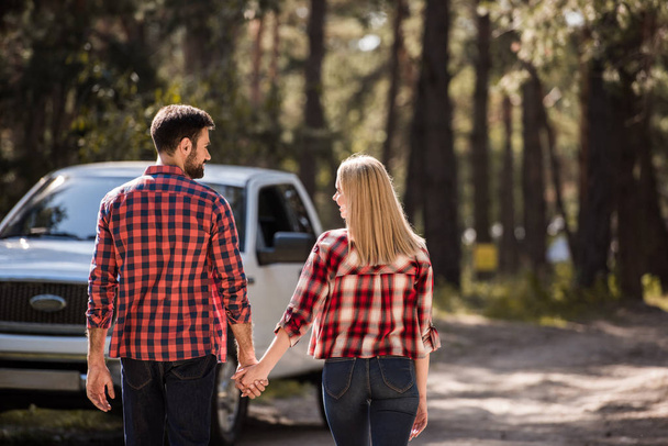 back view of couple holding hands and going to pickup truck in forest - Foto, Imagen