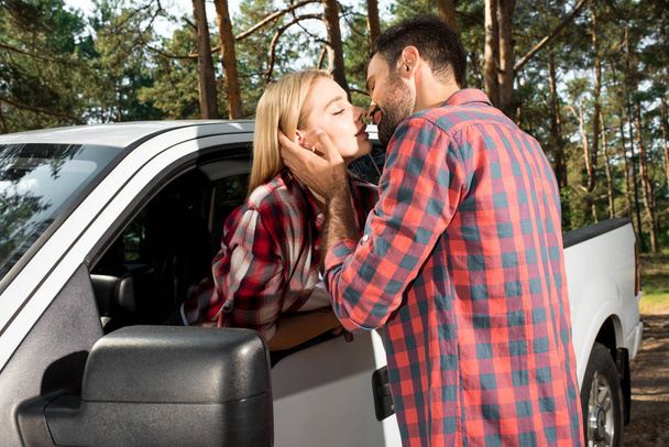 joven hombre besar atractiva novia sentado en recoger coche al aire libre
  - Foto, Imagen