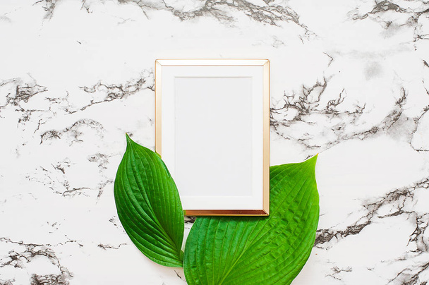 Gold photo frame with tropical leaves on marble background. Mock up frame with copyspace. Flat lay, top view. - Foto, Bild