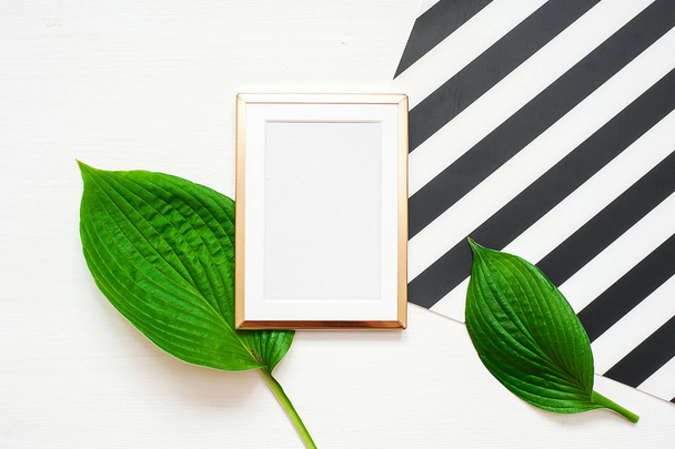 Gold photo frame with tropical leaves on black and white striped background. Mock up frame with copyspace. Flat lay, top view. - 写真・画像