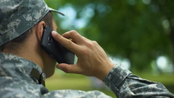 Young male in military uniform talking on phone sitting in park, communication - Footage, Video