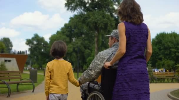Soldiers wife assisting disabled husband in wheelchair, family rest in park - Filmagem, Vídeo